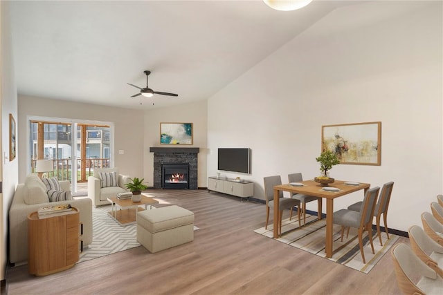 living room with ceiling fan, a fireplace, baseboards, lofted ceiling, and light wood-style floors
