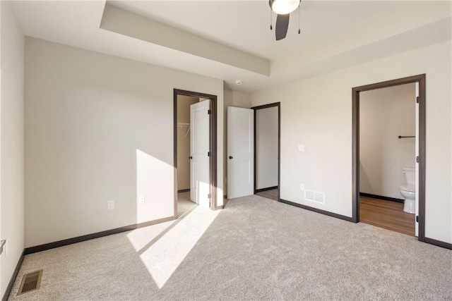 unfurnished bedroom featuring visible vents, a walk in closet, a tray ceiling, and light colored carpet