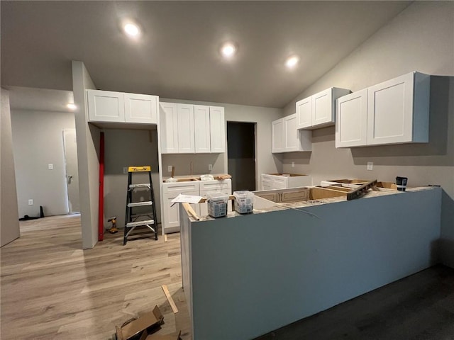 kitchen featuring white cabinets, vaulted ceiling, and light wood-style floors