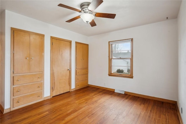 unfurnished bedroom featuring ceiling fan, two closets, and hardwood / wood-style flooring