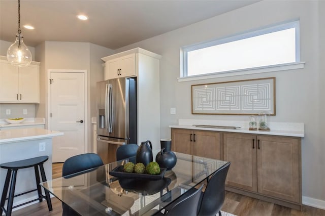 kitchen with light hardwood / wood-style flooring, white cabinets, stainless steel fridge with ice dispenser, a center island, and hanging light fixtures