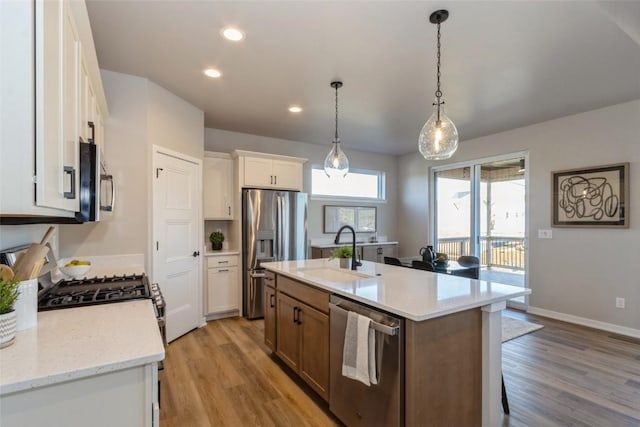 kitchen with light stone counters, appliances with stainless steel finishes, a kitchen island with sink, white cabinets, and light wood-type flooring