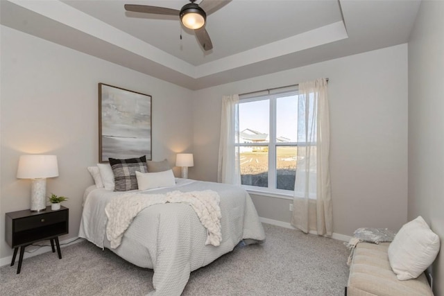 carpeted bedroom with a raised ceiling and ceiling fan