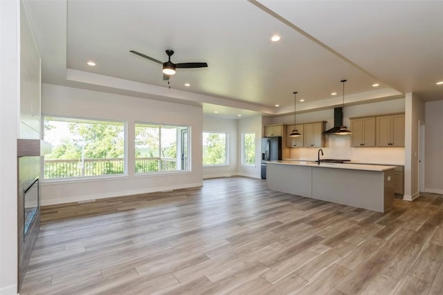 kitchen with stainless steel fridge, an island with sink, light hardwood / wood-style floors, and wall chimney range hood