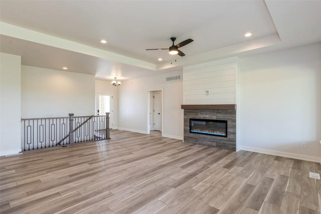 unfurnished living room featuring ceiling fan with notable chandelier, light hardwood / wood-style floors, and a raised ceiling