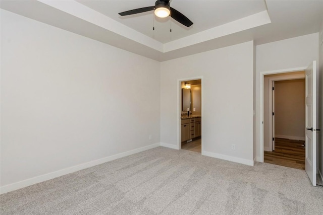 unfurnished bedroom featuring ensuite bathroom, ceiling fan, light colored carpet, and a tray ceiling