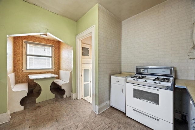 kitchen with light parquet floors, white cabinets, and white gas range oven