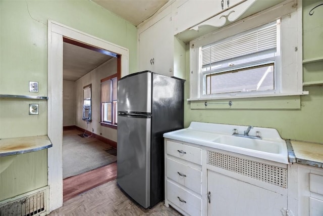 kitchen with white cabinets, sink, stainless steel refrigerator, and light parquet flooring