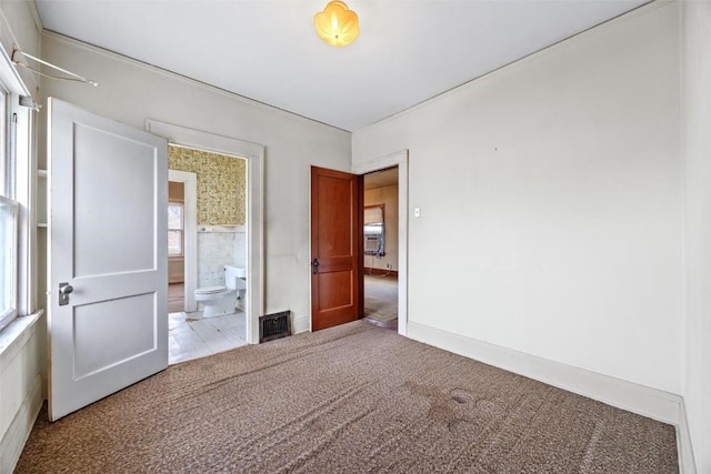 unfurnished bedroom featuring light carpet, ensuite bathroom, and multiple windows