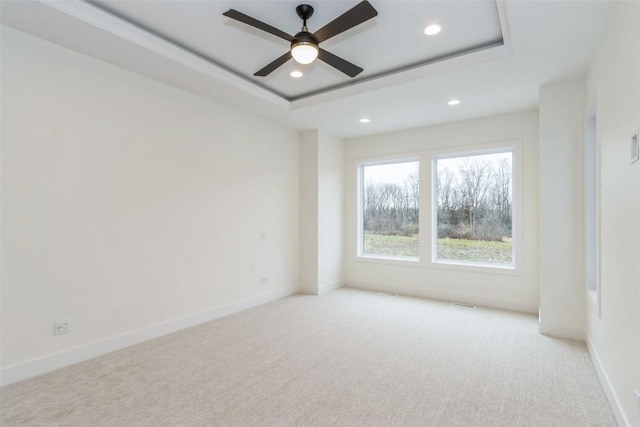 spare room featuring a tray ceiling, ceiling fan, and light carpet