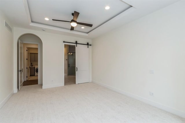 unfurnished bedroom with light carpet, a raised ceiling, ceiling fan, a barn door, and washer / clothes dryer