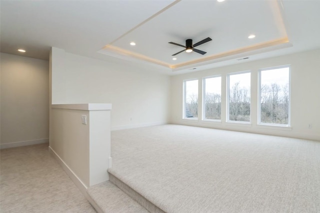 carpeted empty room with a raised ceiling and ceiling fan