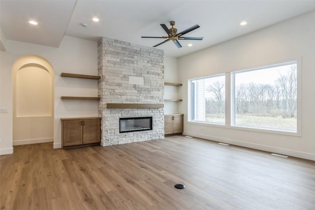 unfurnished living room with a healthy amount of sunlight, a stone fireplace, and light hardwood / wood-style flooring