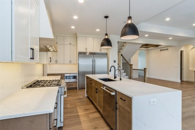 kitchen featuring hanging light fixtures, built in appliances, a large island, light stone counters, and white cabinetry