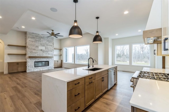 kitchen with sink, hanging light fixtures, light hardwood / wood-style flooring, an island with sink, and custom range hood