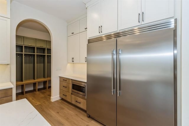 kitchen with light wood-type flooring, built in appliances, and white cabinetry