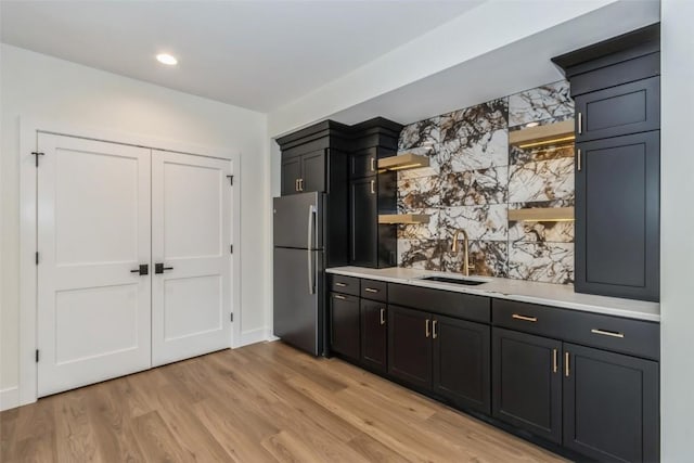 kitchen with stainless steel fridge, light wood-type flooring, sink, and tasteful backsplash