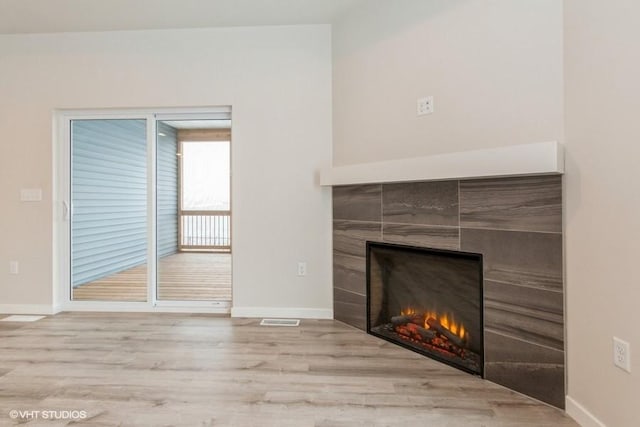 unfurnished living room with a tile fireplace and light wood-type flooring