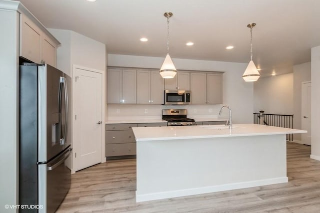 kitchen featuring stainless steel appliances, sink, pendant lighting, light hardwood / wood-style floors, and an island with sink