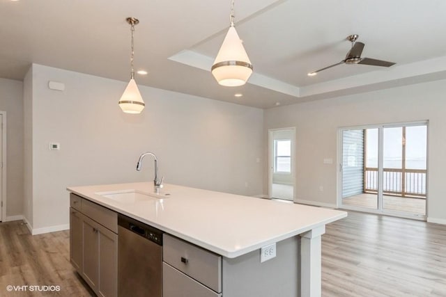 kitchen featuring dishwasher, sink, hanging light fixtures, light hardwood / wood-style flooring, and a kitchen island with sink