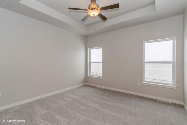 carpeted spare room featuring ceiling fan, a healthy amount of sunlight, and a raised ceiling