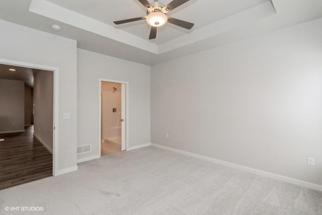 empty room featuring ceiling fan, a raised ceiling, and carpet floors