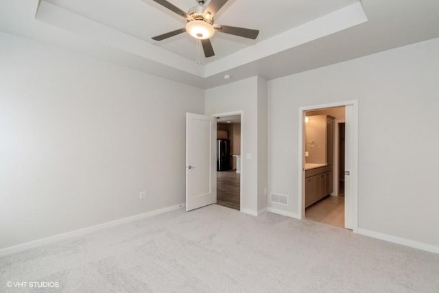 unfurnished bedroom featuring a raised ceiling, connected bathroom, ceiling fan, and light colored carpet