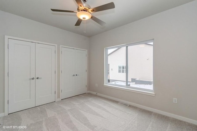 unfurnished bedroom with two closets, light colored carpet, and ceiling fan