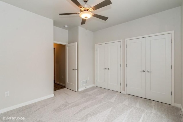 unfurnished bedroom with multiple closets, ceiling fan, and light colored carpet