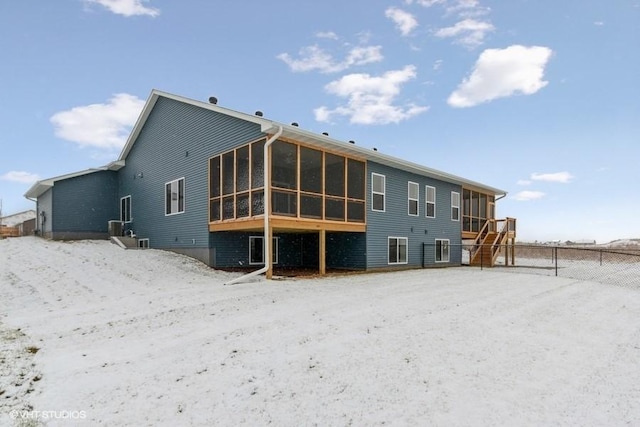 snow covered rear of property with a sunroom