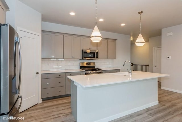 kitchen featuring sink, stainless steel appliances, light hardwood / wood-style floors, pendant lighting, and a kitchen island with sink