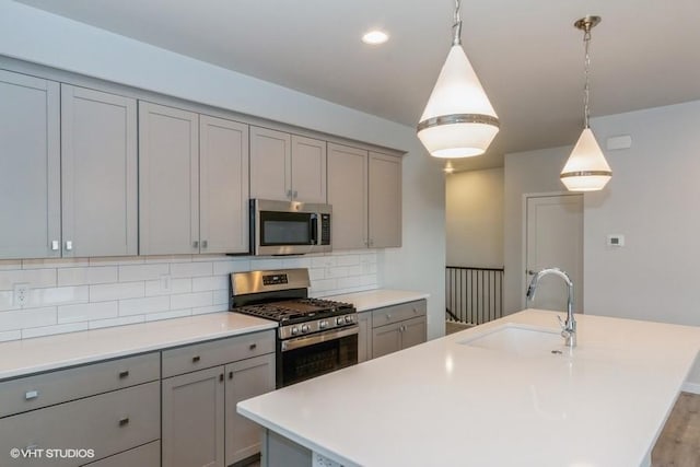 kitchen with sink, stainless steel appliances, gray cabinets, and an island with sink