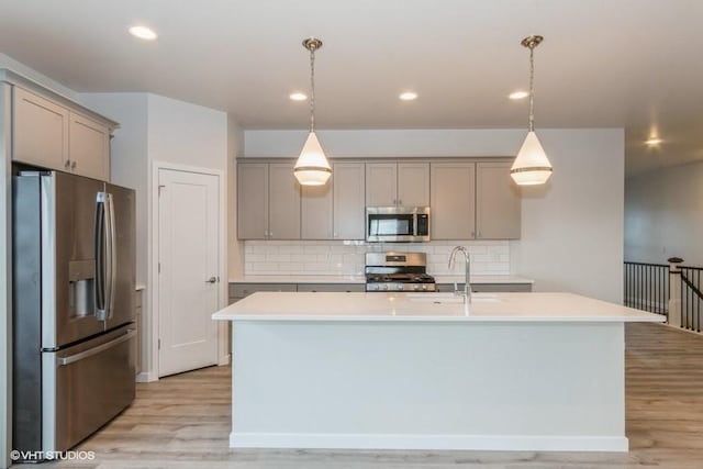 kitchen with sink, an island with sink, hanging light fixtures, and appliances with stainless steel finishes