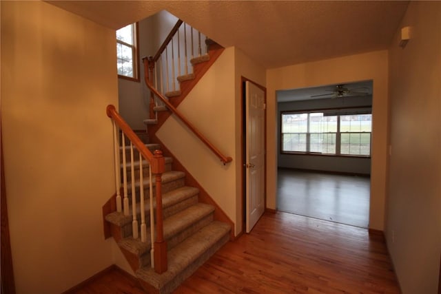 staircase with ceiling fan and wood-type flooring