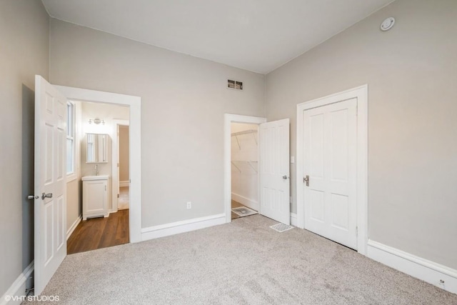 unfurnished bedroom with dark colored carpet and a walk in closet