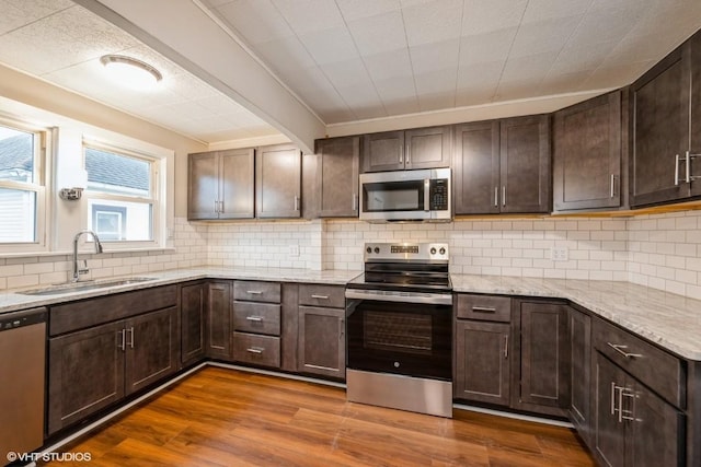 kitchen featuring dark wood-type flooring, sink, dark brown cabinets, light stone counters, and stainless steel appliances