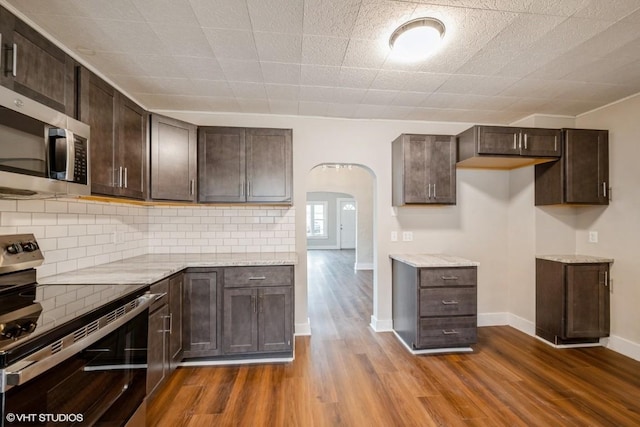 kitchen featuring dark brown cabinetry, stainless steel appliances, light stone counters, and dark hardwood / wood-style floors