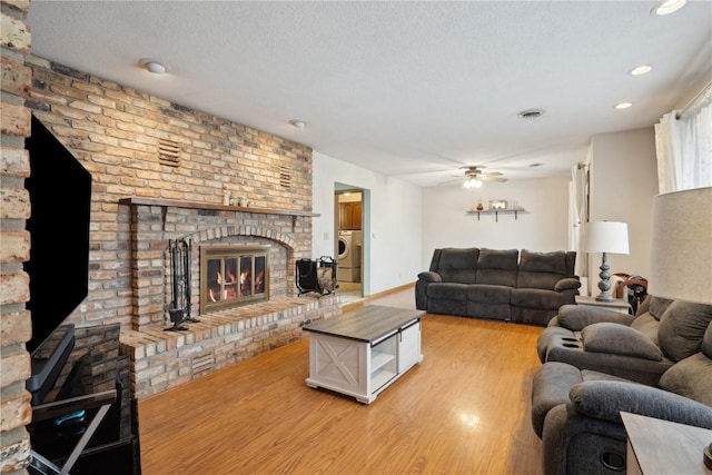 living room with ceiling fan, light hardwood / wood-style floors, a textured ceiling, washer / dryer, and a fireplace