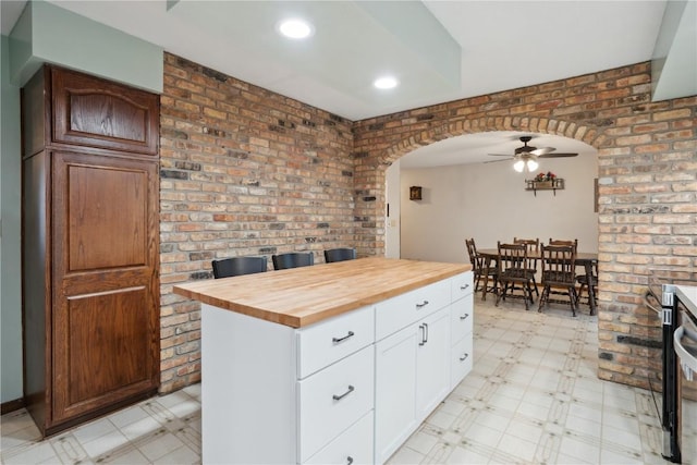 kitchen featuring wood counters, a center island, ceiling fan, white cabinetry, and brick wall