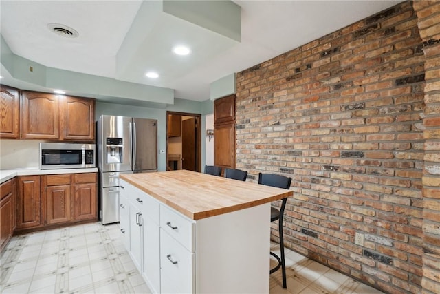 kitchen featuring wood counters, appliances with stainless steel finishes, brick wall, a center island, and a breakfast bar area