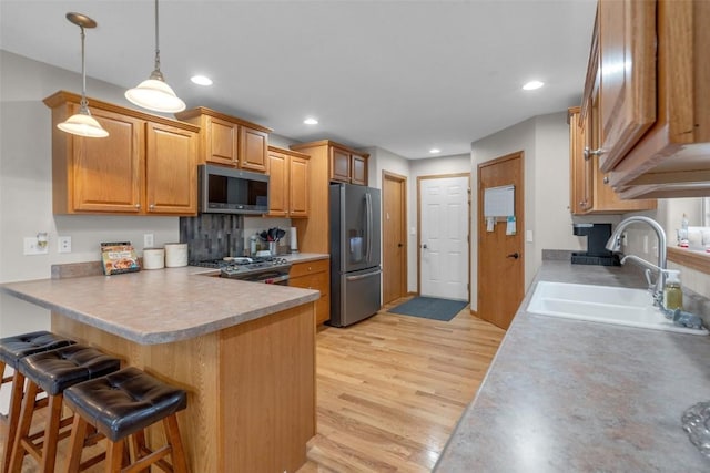 kitchen with a kitchen bar, light wood-type flooring, stainless steel appliances, sink, and pendant lighting