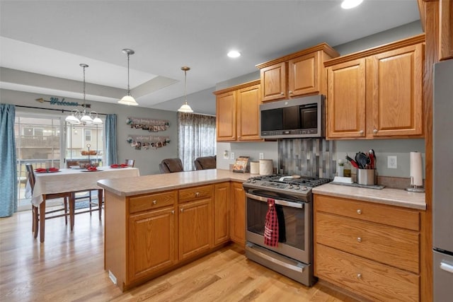 kitchen featuring kitchen peninsula, a chandelier, light hardwood / wood-style floors, pendant lighting, and appliances with stainless steel finishes