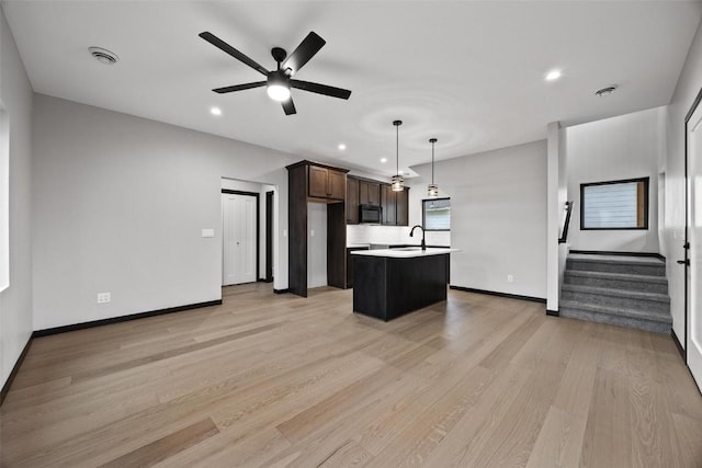 kitchen with dark brown cabinetry, ceiling fan, a center island with sink, light hardwood / wood-style flooring, and hanging light fixtures