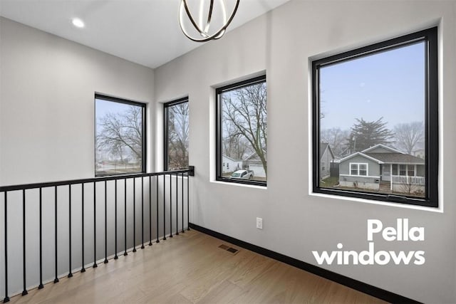 empty room with a wealth of natural light, light hardwood / wood-style flooring, and a chandelier