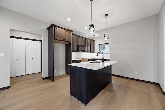 kitchen with a center island with sink, sink, hanging light fixtures, light hardwood / wood-style floors, and dark brown cabinetry