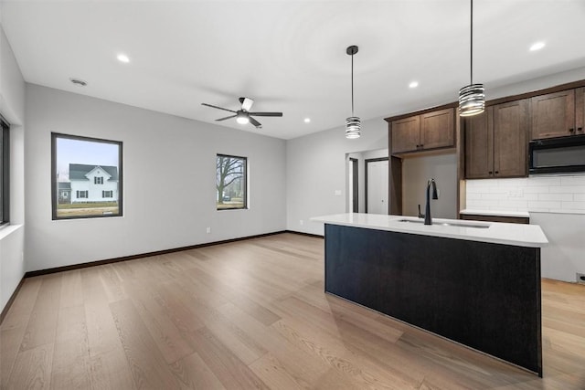 kitchen featuring pendant lighting, backsplash, a center island with sink, sink, and dark brown cabinets