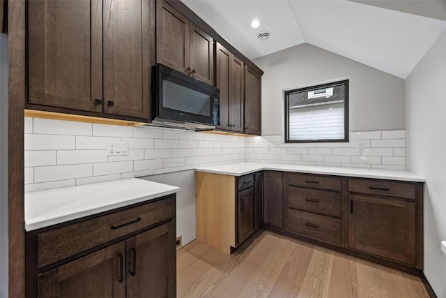 kitchen featuring dark brown cabinets, light hardwood / wood-style floors, and vaulted ceiling