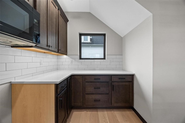 kitchen featuring dark brown cabinets, light hardwood / wood-style floors, vaulted ceiling, and tasteful backsplash