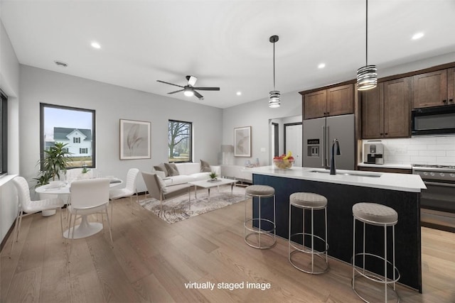 kitchen featuring a center island with sink, hanging light fixtures, decorative backsplash, dark brown cabinetry, and stainless steel appliances