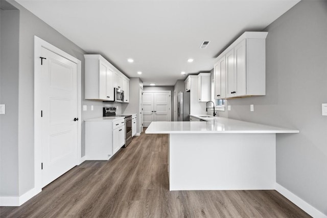 kitchen with kitchen peninsula, stainless steel appliances, white cabinetry, and dark wood-type flooring